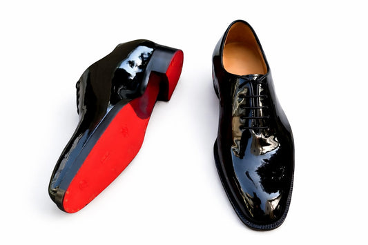 Black patent leather dress shoe with red sole on a white background