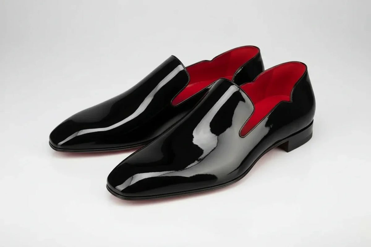 Black glossy loafers with red lining on a white background